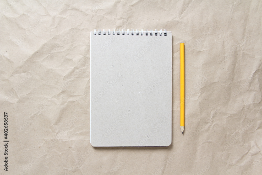 Gray notepad with white coiled spring and pencil on a background of beige crumpled craft paper. With empty space for text and design Gray notepad with white coiled spring and pencil on a background of beige crumpled craft paper. With empty space for text and design