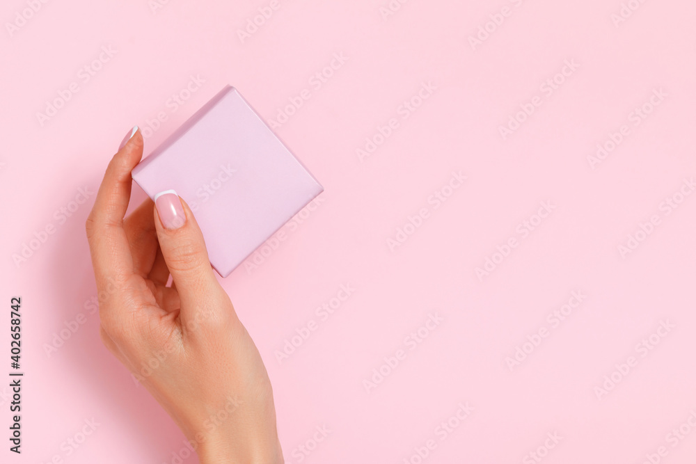 A female hand holds a gift box on a pink pastel background. Birthday valentine's day new year christmas. Copy space.