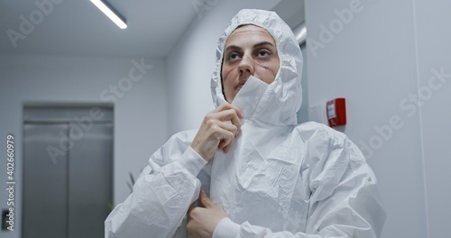 Exhausted nurse putting on hazmat PPE suit in hospital. Covid-19 coronavirus pandemic concept.