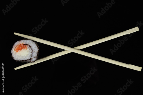 chopstick holding a sushi roll with salmon or trout