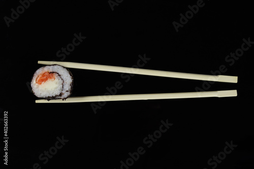 chopstick holding a sushi roll with salmon or trout