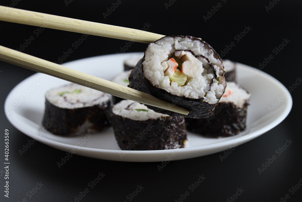 chopstick holding a sushi roll with cucumber and crab stick chopstick holding a sushi roll with cucumber and crab stick