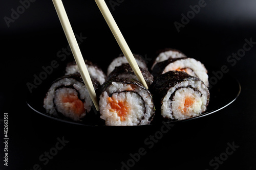 chopstick holding a sushi roll with salmon or trout