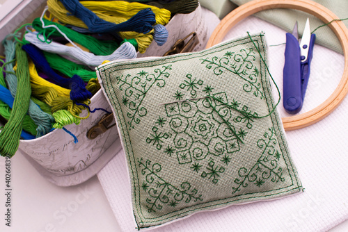 A pillow with embroidery lies next to a box of thread