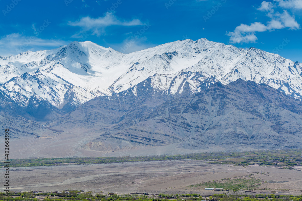 Beautiful landscape with fields of delta of Indus River, Tibetian buildings, Himalayas snow mountains, and blue sky,  in Ladakh, Kashmir, view from Thiksey Monastery or Thiksey Gompa.