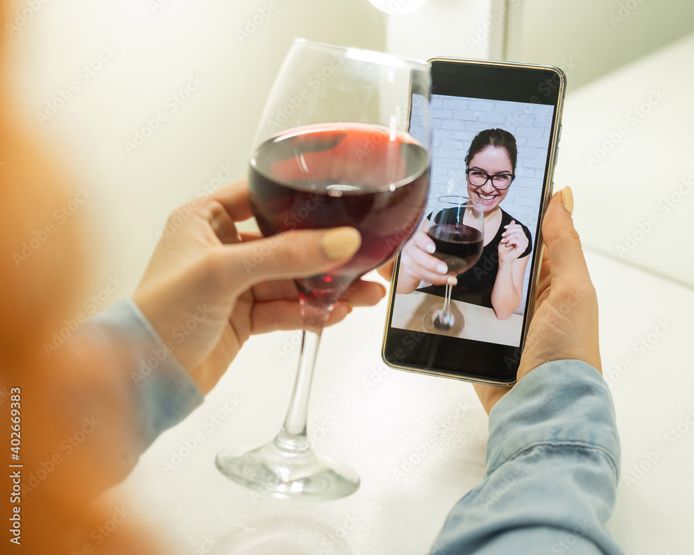 The women talk over video communication on the phone and drink red wine. The quarantined girl is not making a video call