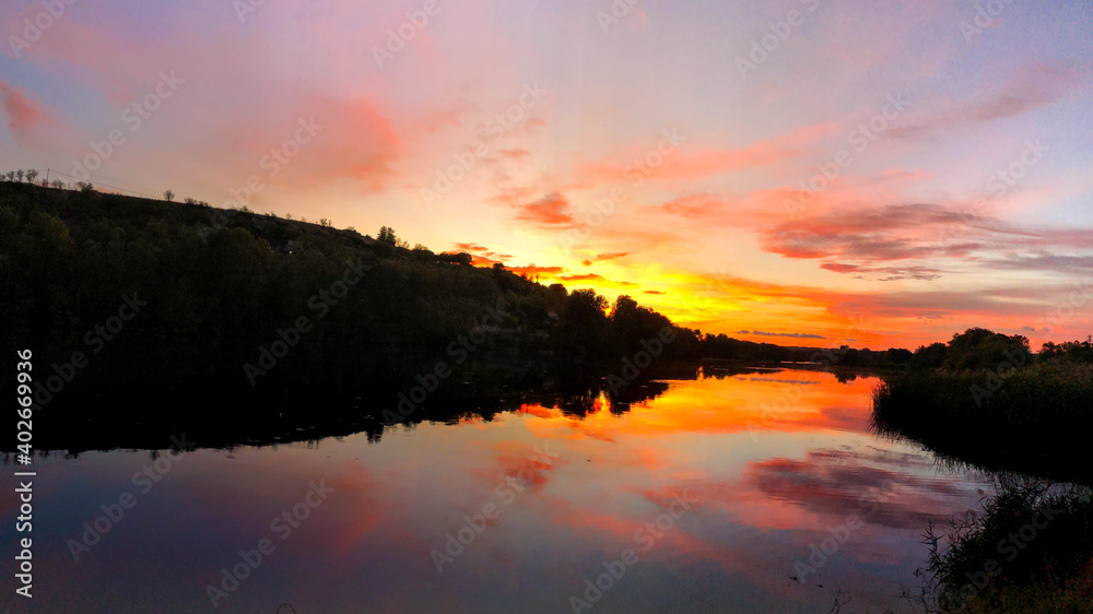 Very dramatic sunset scene. Colours red, orange, violet and reflections in the water. Horizontal panoramic view of a sunset