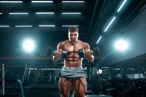 Bodybuilder athlete man pumping up muscles in the gym. Brutal strong muscular guy on fitness workout. Bodybuilding concept.