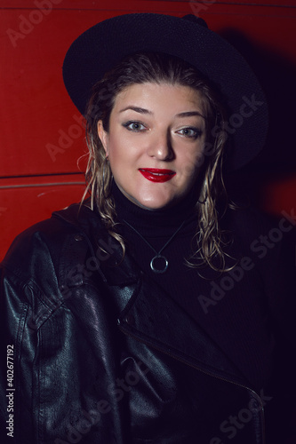 woman in black hat and leather jacket on red background