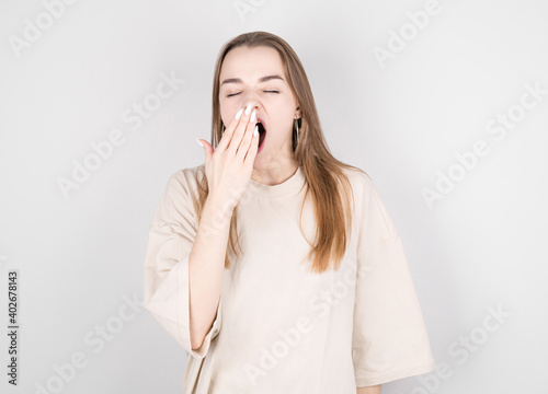 Young girl yawns from fatigue near the gray wall