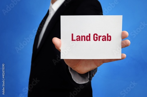 Land Grab. Lawyer (man) holding a card in his hand. Text on the sign presents term. Blue background. photo