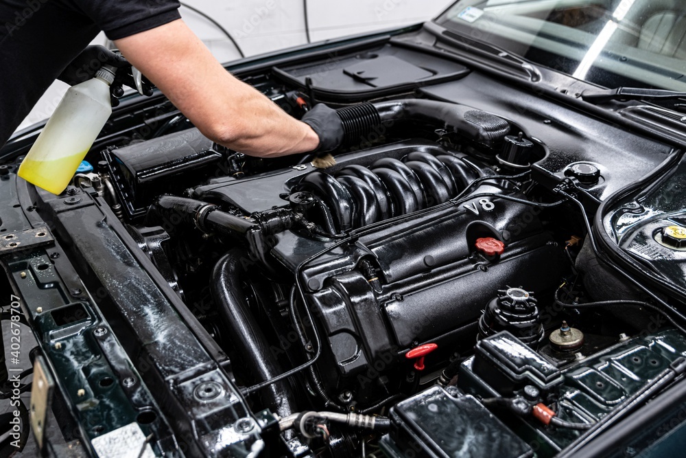 Car wash worker carefully cleaning engine with a brush