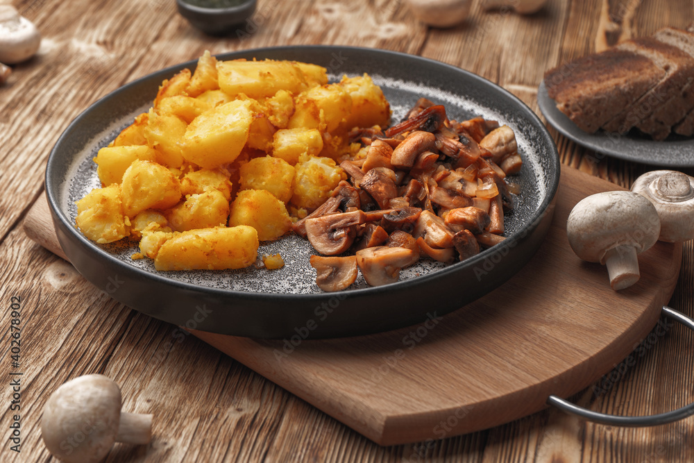 Vegetarian fried potatoes with mushrooms on a concrete plate on a wooden plank table. Vegetarian fried potatoes with mushrooms on a concrete plate on a wooden plank table.