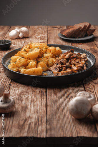 Fried potatoes with mushrooms on a wooden rustic table near fresh mushrooms