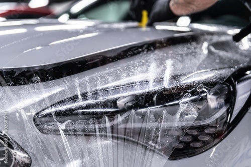Obraz na płótnie Car detailing studio worker applying protective ppf foil film on car body and lamps w salonie