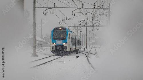 Modern commuter passenger train is rushing through the dense snowfall or snow which is hindering drivers sight. Urban city setting photo