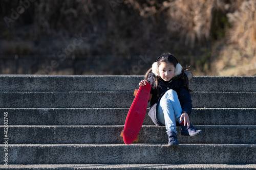 スケートボードを持って階段に座る少女