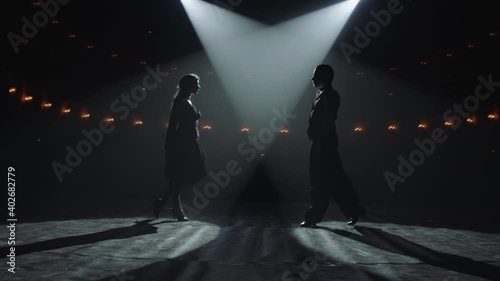 Attractive couple of ballroom dancers dancing passionate latin american dance cha cha cha. Silhouettes of two dancers on a smoky Stage with spot light. Anamorfic lens