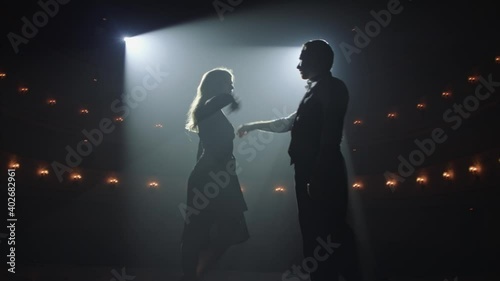 Attractive couple of ballroom dancers dancing passionate latin american dance cha cha cha. Silhouettes of two dancers on a smoky Stage with spot light. Anamorfic lens