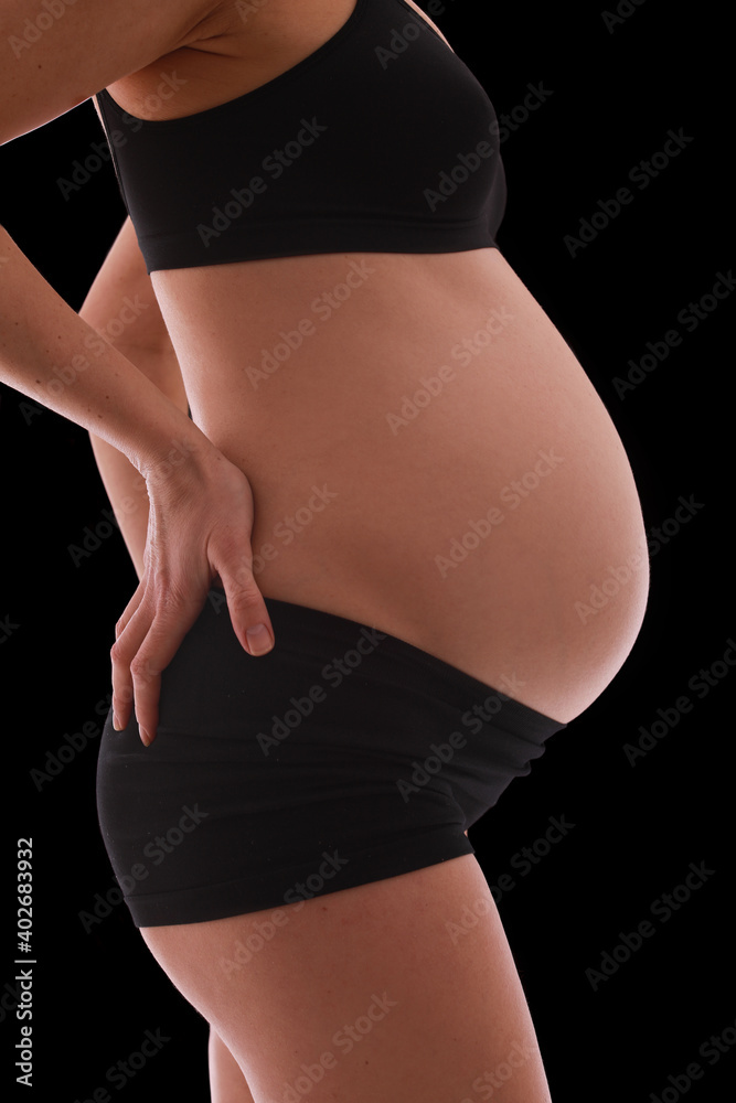 Fototapeta premium close up view of pregnant belly. Woman in black underwear isolated on black background.