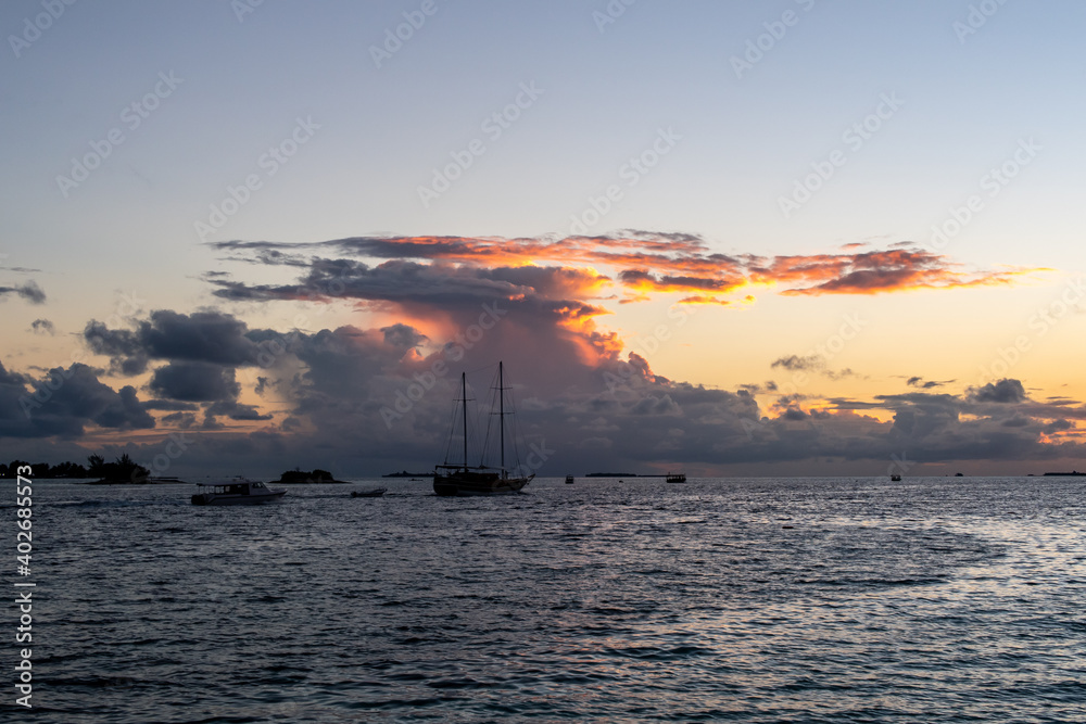 Wooden ship sailing with cumulonimbus thunderstorm clouds and sunset in the background, Maldives.