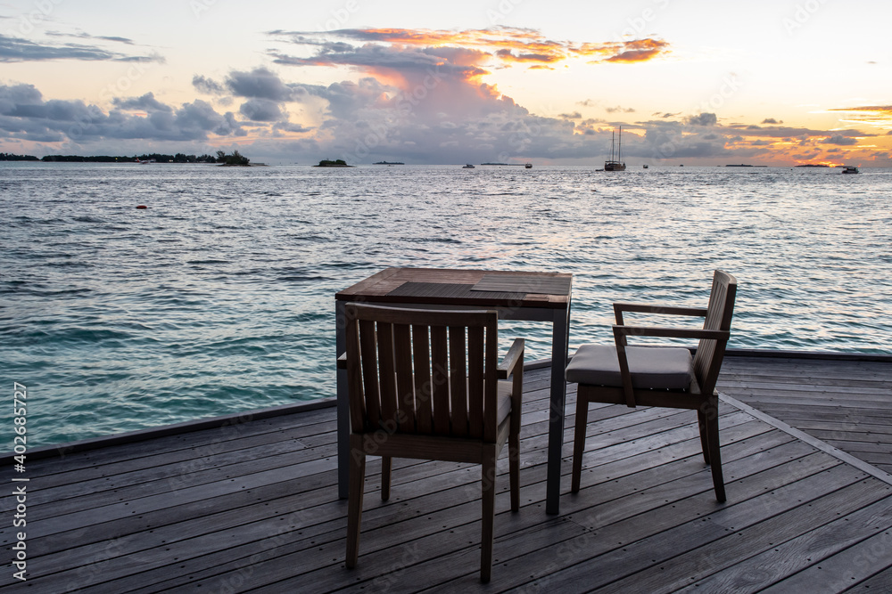 Wodden dining table on a terrace overlooking the sea, with sunset in the background, Maldives. Wodden dining table on a terrace overlooking the sea, with sunset in the background, Maldives.