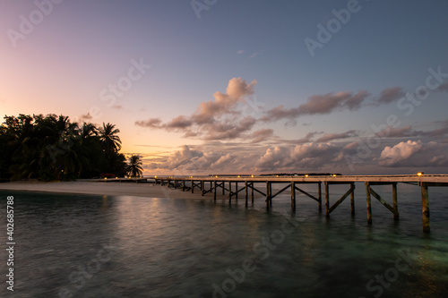 Wooden jetty with lanterns over the ocean extending from tropical island, with blurred water and sunset in the background, Maldives, long exposure.
