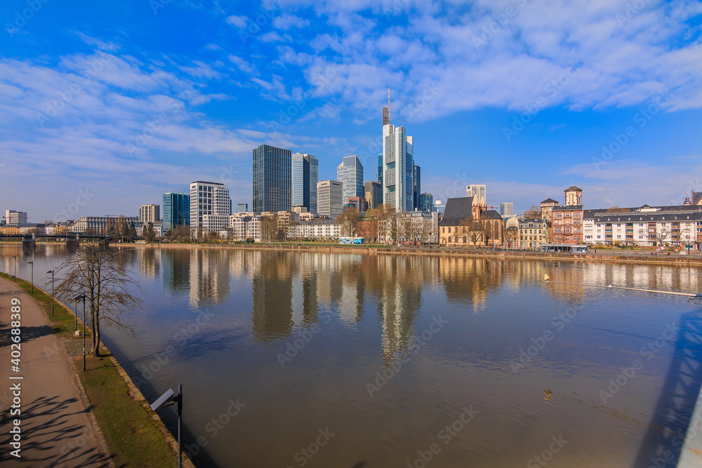 Financial district with skyscraper of Frankfurt am Main. River with reflections in the foreground on a sunny day. Bank on the river in spring