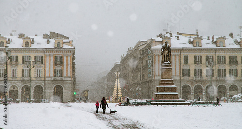 piazza cittadina con mamma, bimba e cane che passeggiano sotto una fitta nevicata