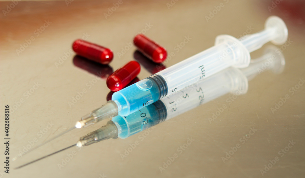 Syringe next to three red capsules Syringe next to three red capsules