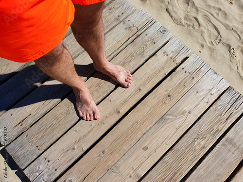 Male feet and Wooden boardwalk on the sandy beach. Top view.