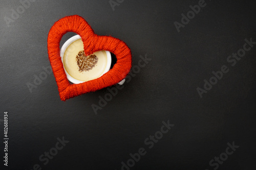 On a cup of cappuccino a red heart on a black background with a place for the text.