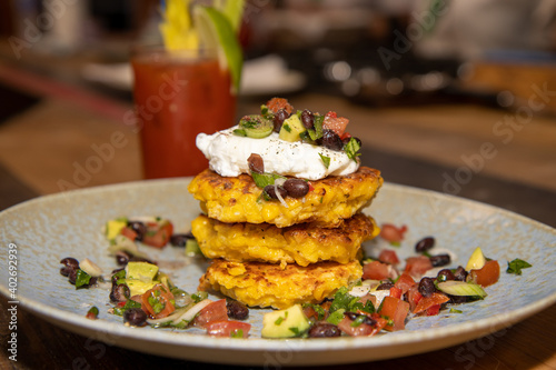 A plate of delicious sweetcorn fritters with a bloody mary drink on a kitchen wooden work top