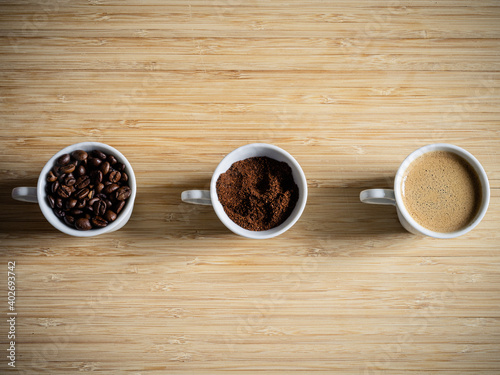 3 Tassen mit Kaffeebohnen, Kaffeepulver, Kaffee auf Holzbrett