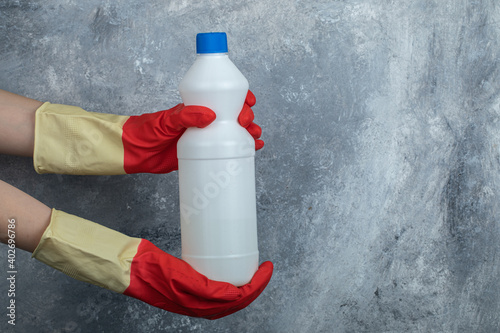 Hands in red gloves holding container of bleach photo