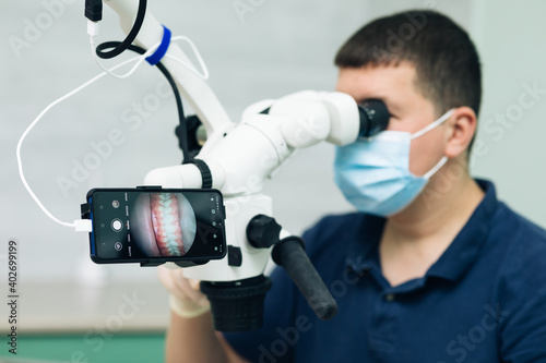 Dentist is treating patient in modern dental office. Doctor making teeth examination research survey using microscope in dentistry.
