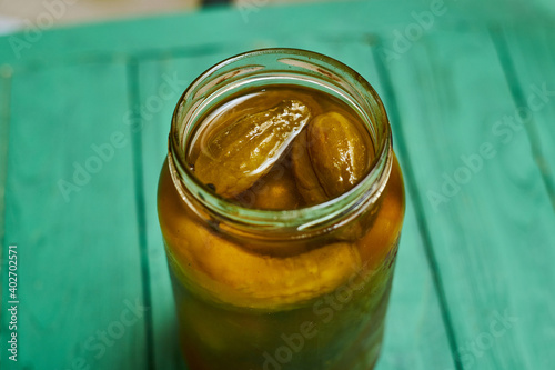 Pickled, canned cucumbers in a jar on a green background.