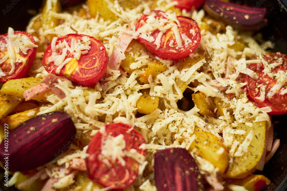 Fototapeta premium Baked potato with meat, tomatoes, beetroot in the oven. Sprinkled with cheese.