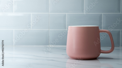 A pastel pink coffee cup or mug glass is placed on marble floor with space of brick tile as background. Photo applied extra exposure as sunlight and high contrast ration. Selective focus.