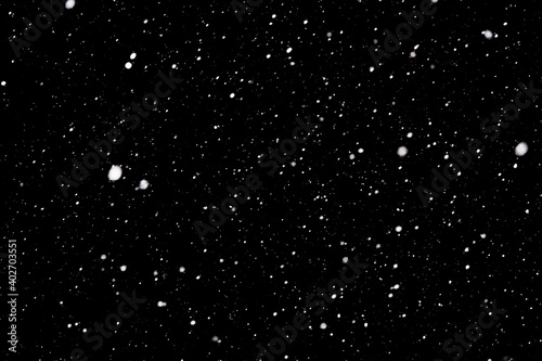 Falling snowflakes on a black background. The texture of the snow. Snowstorm. Element for the design. The bokeh effect.