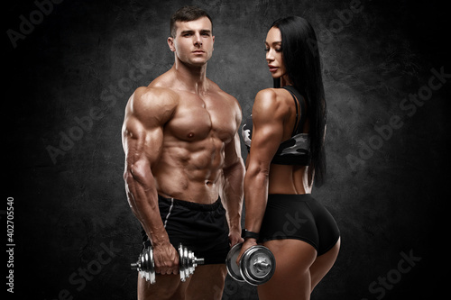 Sporty couple showing muscles on wall background. Muscular man and woman