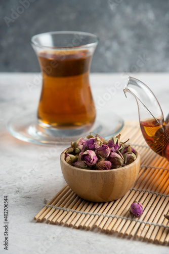 A glass cup of tea with dried roses and teapot