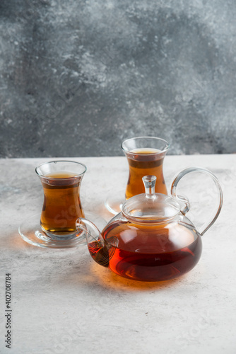 Two glass cup of tea with teapot on a marble background
