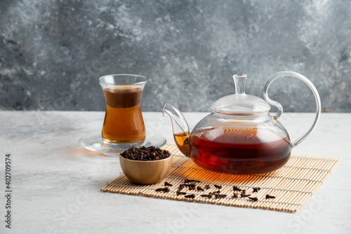 A glass cup of tea with dried cloves and teapot