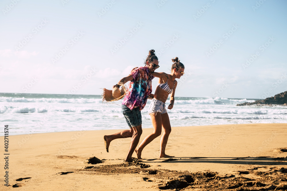 Fototapeta premium Young beautiful couple have fun and laugh at the beach in summer holiday vacation - people and travel lifestyle enjoy the sand and the sun playing together in outdoor leisure activity