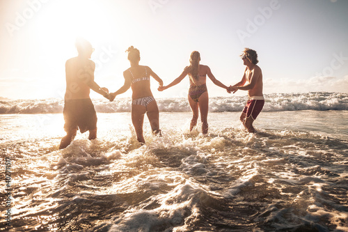 Group of friends enjoy summer holiday vacation at the beach running together in the sea water during a golden sunset - people and travel activity in tropical coast place