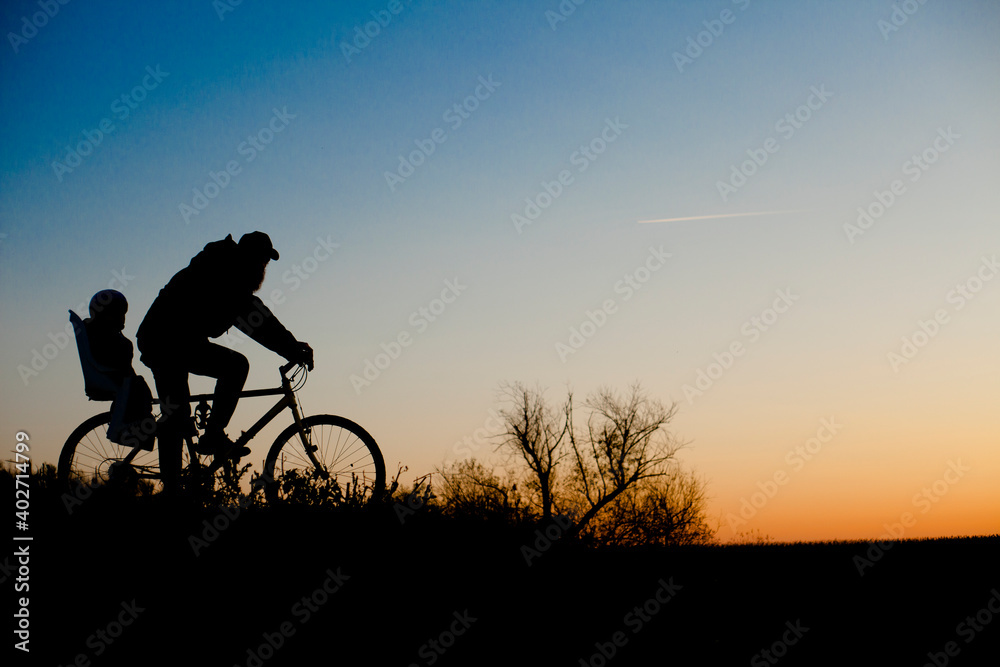 A silhouette of a father and his child ona bicycle during the sunset.