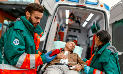 Paramedics check the level of oxygen in the blood and transport the elderly patient's gurney from the modern ambulance for further medical care at the clinic.