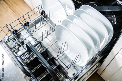 White plates in an open dishwasher, top view. Modern kitchen appliance.