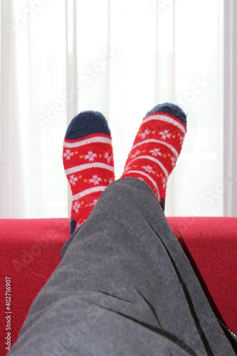 Two feet with warm Christmas socks, crossed on the couch, white light in the back